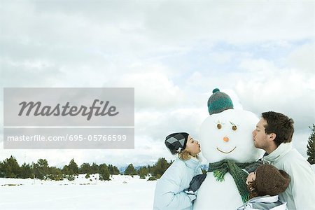 Three young friends kissing snowman, head and shoulders