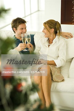 Couple making toast with champagne, smiling at each other, Christmas tree in foreground