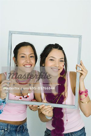 Two young friends holding up frame together, smiling at camera, portrait