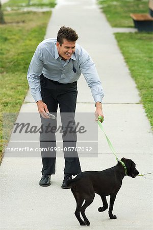 Man walking dog on sidewalk, bending forward, smiling