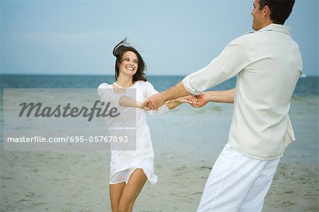 Man and young female companion on beach, holding hands, swinging each other around