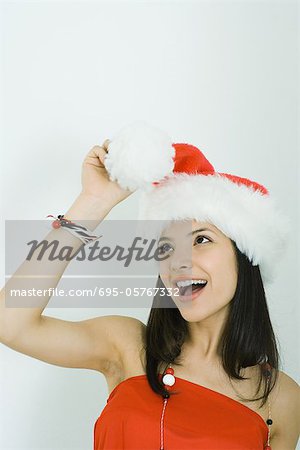 Teenage girl wearing Santa hat, looking up at pom-pom in hand, smiling