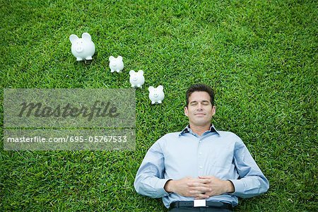 Man lying on grass, line of piggy banks by head