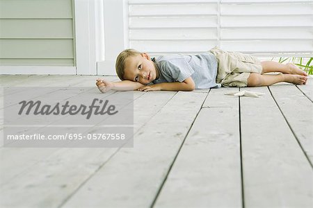 Boy lying on the ground next to starfish, head resting on arm