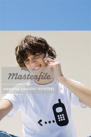 Teenage boy wearing tee-shirt printed with cell phone graphic, using cell phone, smiling at camera