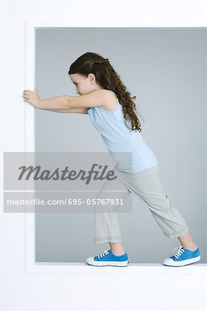 Little girl standing inside window frame, pushing edge, full length