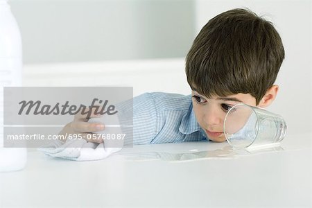 Little boy wiping up spilled milk with towel