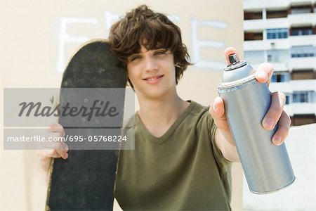 Teen boy holding spray paint can, smiling at camera
