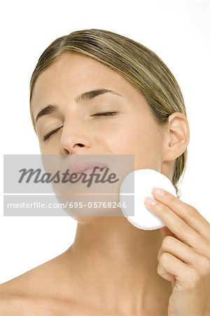 Woman using powder puff on cheek, eyes closed