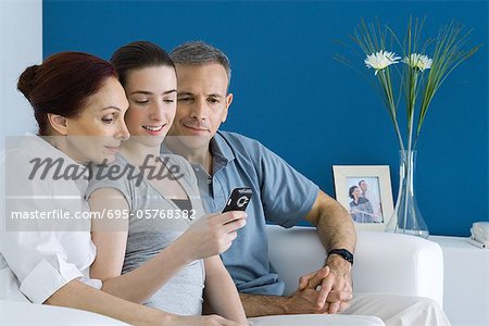 Teen girl on sofa with parents, looking at cell phone together