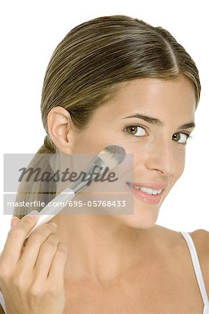 Woman applying face powder with make-up brush, smiling at camera