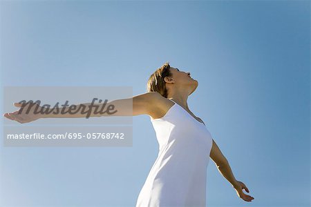 Woman with outstretched arms, looking up, low angle view