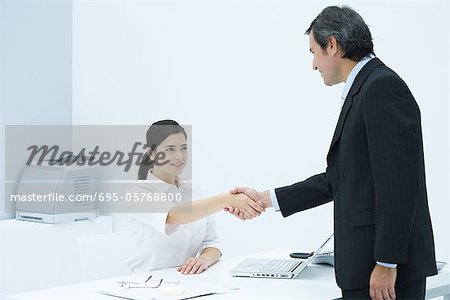 Professional woman sitting at desk, shaking hands with businessman