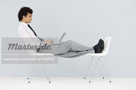 Businessman sitting in chair, feet up on another chair, using laptop