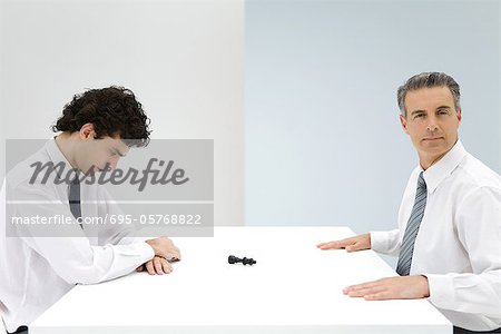 Businessmen sitting at table, tipped over chess piece between them