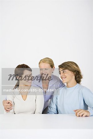 Mature woman embracing younger woman and teen boy, all smiling, portrait