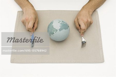 Person sitting before globe on placemat, holding fork and knife, cropped view