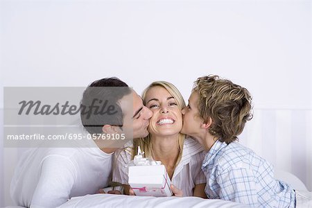 Woman holding a gift, husband and son kissing her on both cheeks