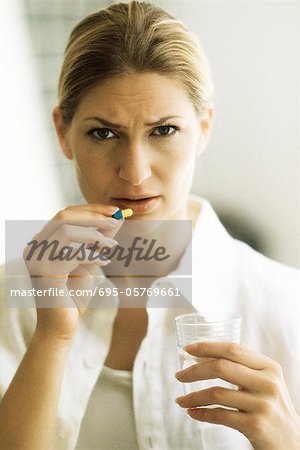 Woman holding pill, frowning at camera