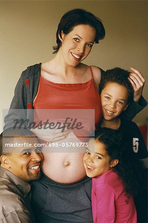 Pregnant woman with family, daughter and husband leaning against her stomach