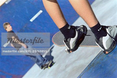 Skateboarder perched at edge of ramp watching friend skate on ramp below