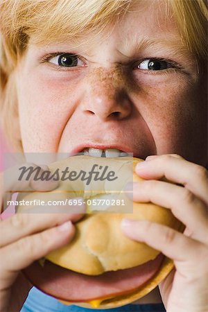 Boy biting into ham and cheese bagel sandwich, close-up