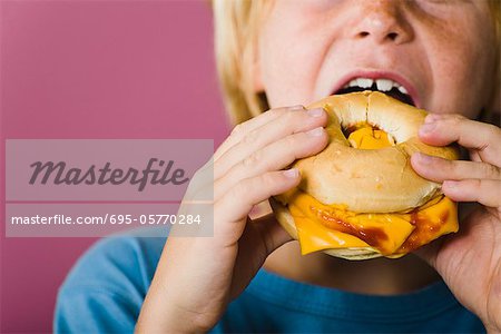 Boy eating bagel and cheese sandwich, cropped Boy eating bagel and cheese sandwich, cropped