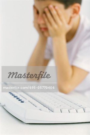 Boy at computer keyboard holding head