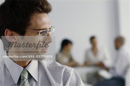 Young businessman in office, turning head to listen to colleagues in background