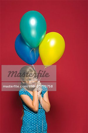 Girl holding balloons, looking away, smiling