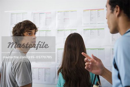 College students chatting, female student checking bulletin board in background