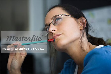 Woman thinking, looking away, pen in mouth