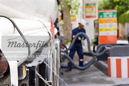 Hoses connected to fuel tanker outlets transferring fuel to gas station storage tanks