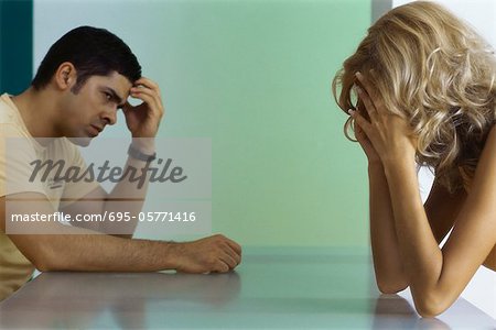 Upset couple sitting at table, both holding heads