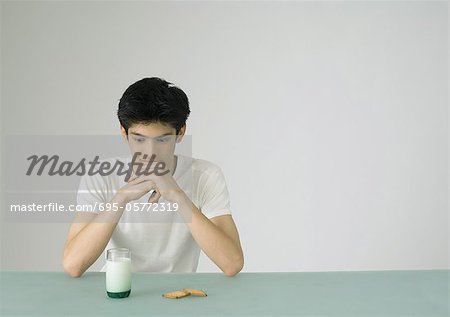 Young man looking at glass of milk and cookies