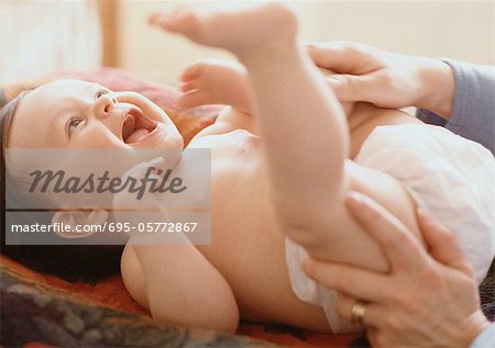 Adult playing with baby lying on table.