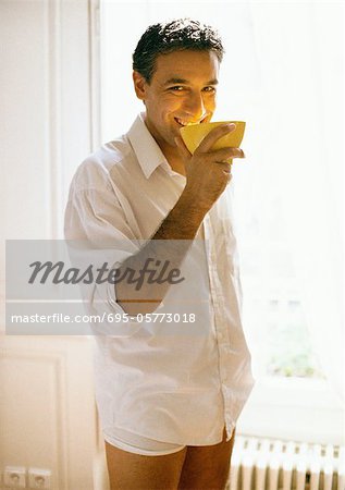 Man wearing buttondown shirt and underwear holding bowl to mouth