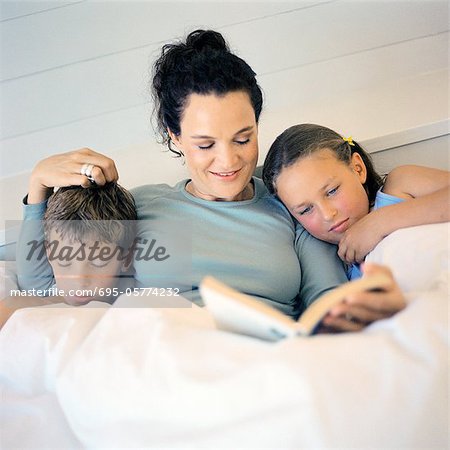 Mother lying in bed between children, reading book
