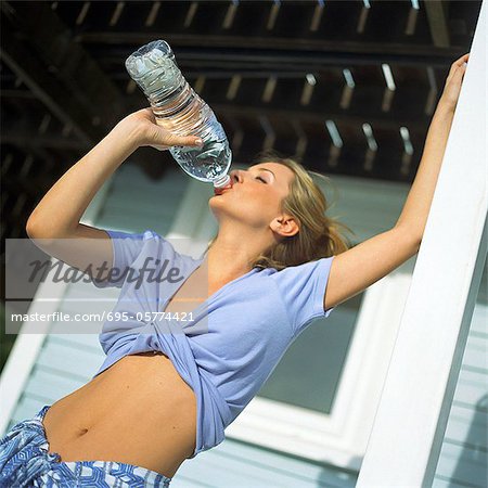 Young woman with bare midriff drinking from plastic bottle, low angle view