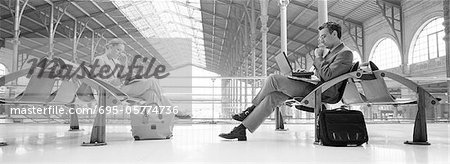 Businesspeople sitting in train station, b&w, panoramic view