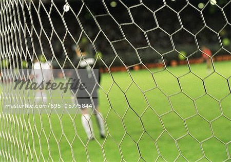 Goal keeper standing in front of goal during a match, blurred, seen from behind net.