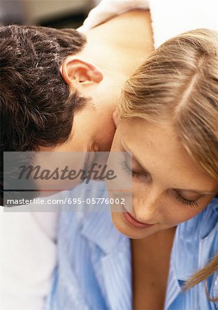 Man leaning over woman's shoulder, kissing woman's neck, close-up