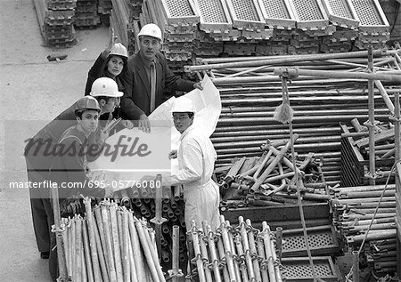Five people examining blueprints in construction site, portrait, b&w
