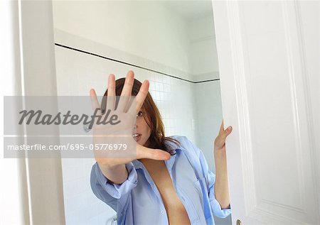Young woman in bathroom, hand out in front of face, closing door