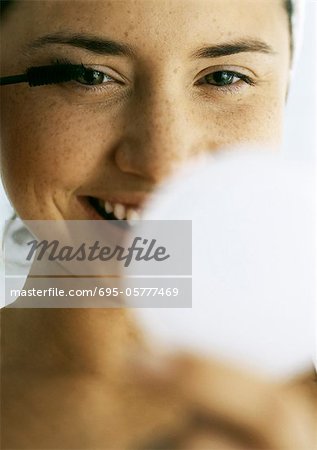 Woman applying mascara, close-up, compact blurred in foreground