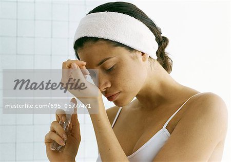 Young woman holding perfume bottle, smelling wrist