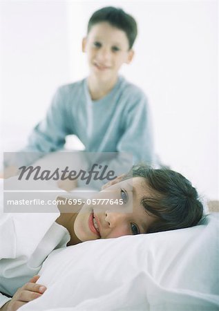 Girl lying in bed looking at camera, boy in background