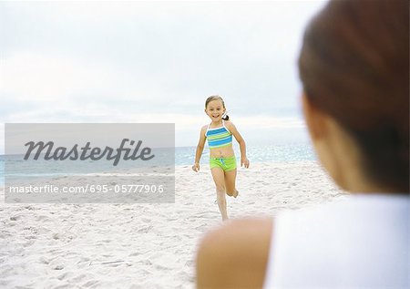 Girl running towards mother on beach