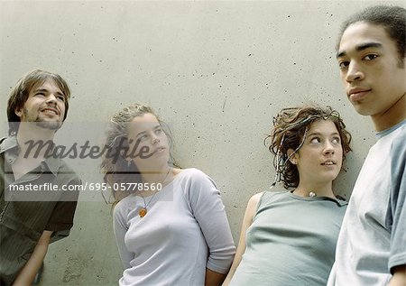 Four young friends standing next to wall
