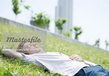 Young man lying on grass in urban park